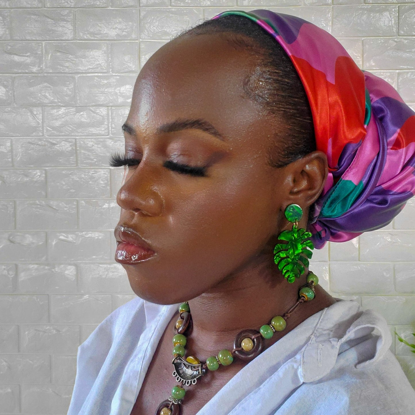 Model closing her eyes as she is wearing a colorful headscarf with pink, red, purple and green