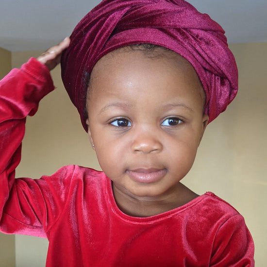 Little girl wearing a red turban and touching her head